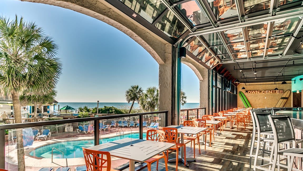 A covered outdoor seating area with a pool and ocean view.