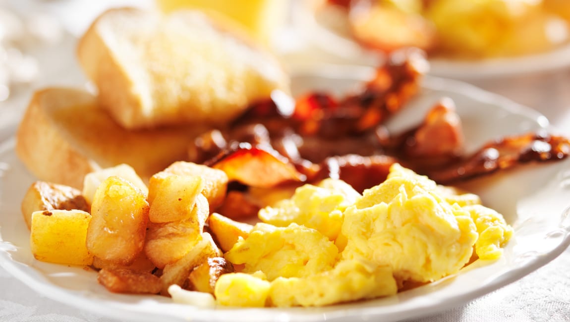 a plate of breakfast food with scrambled eggs, potatoes, bacon, and toast