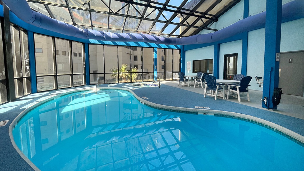 A large indoor pool with a glass ceiling and blue walls, surrounded by seating areas.