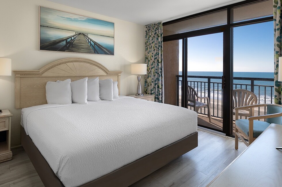 A hotel room with a large bed, balcony, and ocean view.