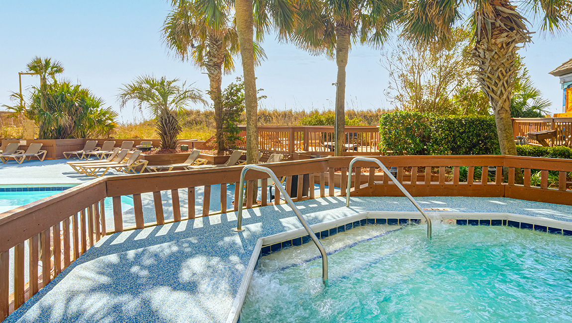 A swimming pool with a wooden fence and palm trees in the background.